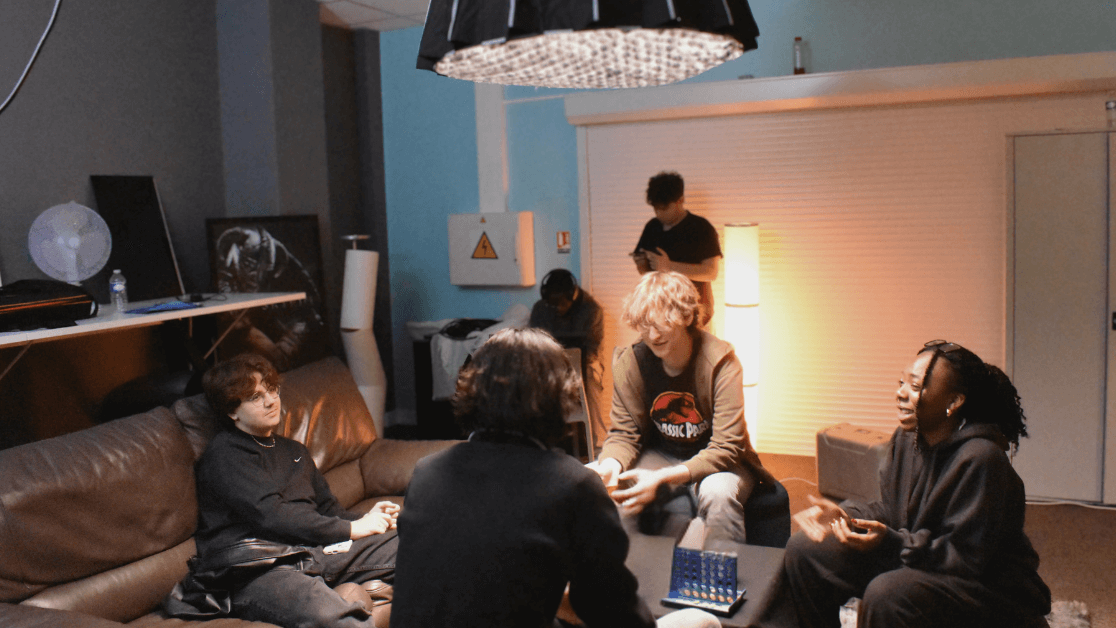 Moment de convivialité entre étudiants au campus de la SAE Institute Groupe d'étudiants de la SAE Institute discutant dans un espace détente du campus, ambiance chaleureuse et créative.